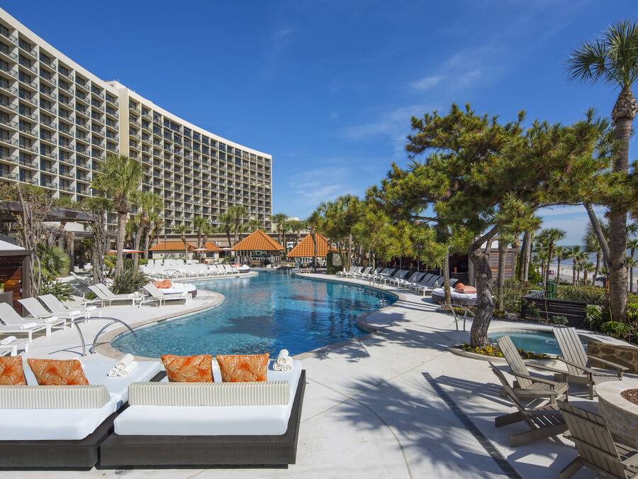Un espace piscine d’hôtel comprenant des chaises longues, une grande piscine et un bâtiment doté de balcons.