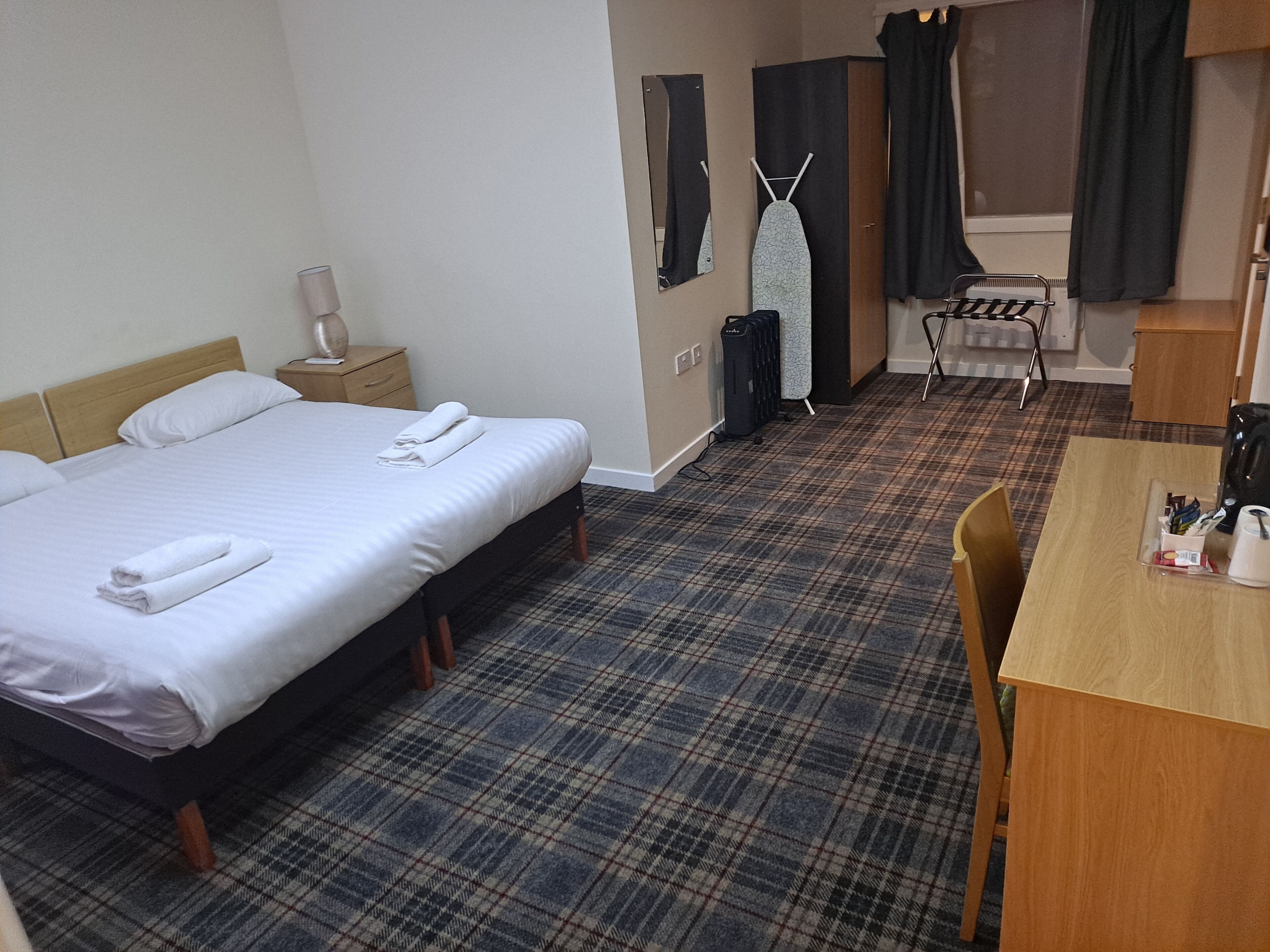 A hotel room with a large bed, a small desk, a chair, a wardrobe, an ironing board, and a mirror.