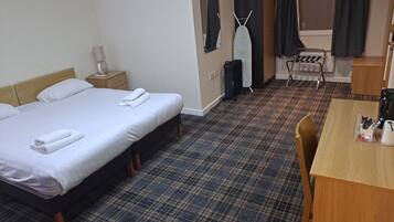 Habitación de hotel con una cama grande, un escritorio pequeño, una silla, un armario, una tabla de planchar y un espejo.