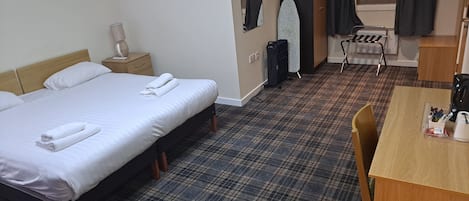 A hotel room with a large bed, a small desk, a chair, a wardrobe, an ironing board, and a mirror.