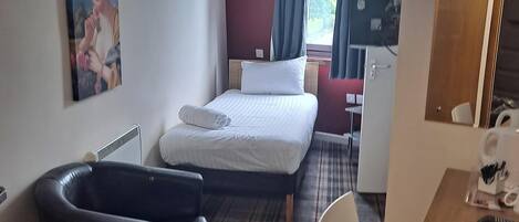 A hotel room with a bed, a black bathtub, a desk with a chair, a painting on the wall, and a window with curtains.
