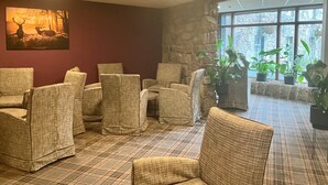 A room with wicker chairs arranged in a semi-circle, a stone wall, and a large window with plants.