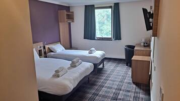 Habitación de hotel con dos camas, un escritorio pequeño, una ventana con cortinas y una alfombra estampada en cuadros.