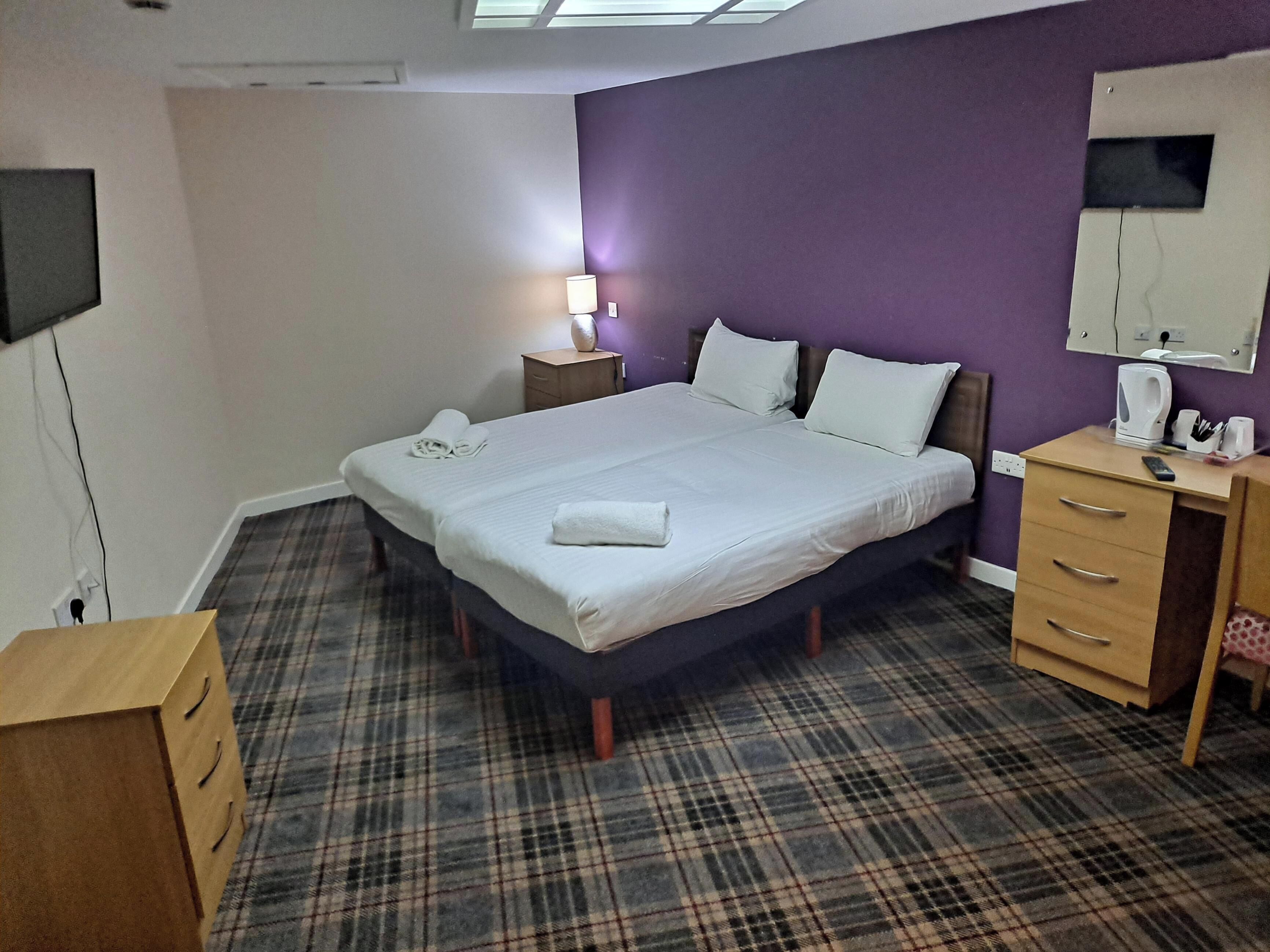 A hotel room with a large bed, a desk, a chair, a TV, and a window.