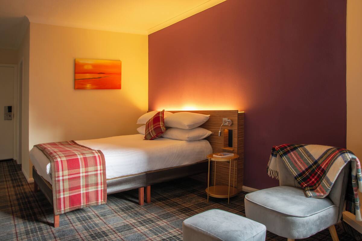 A neatly arranged hotel room with a bed, a chair, and a small table.