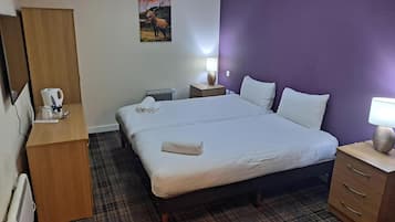 A hotel room with a bed, a desk, a chair, a radiator, a lamp, and a painting on the wall.