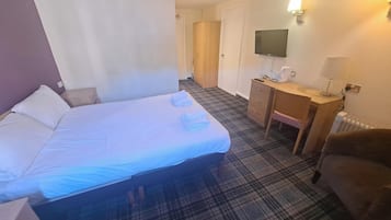 A hotel room with a bed, a desk, a chair, a television, and a radiator.