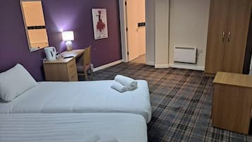 A hotel room with two beds, a desk, a chair, a wardrobe, and a painting on the wall.