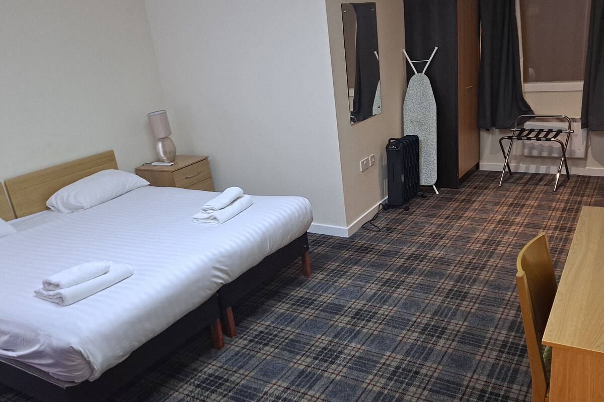 A hotel room with a bed, a bedside table, a lamp, a chair, a desk, and a mirror.