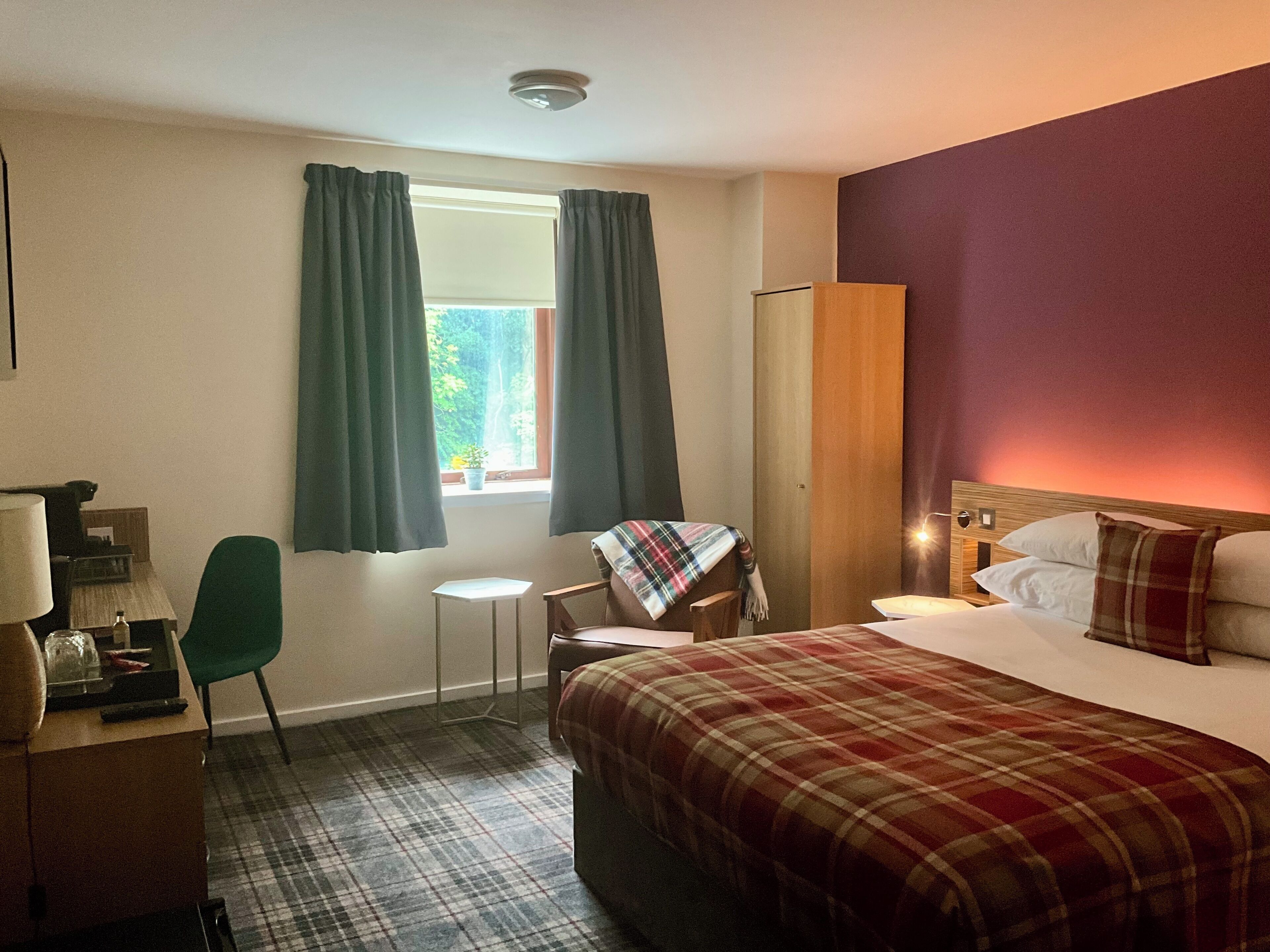 Ein Hotelzimmer mit Bett, Schreibtisch, Stuhl, kleinem Tisch und einem Fenster mit Vorhängen.