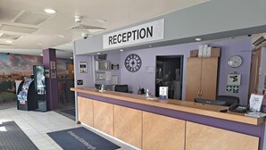 A reception area with a sign labeled "RECEPTION," a clock, a computer, and a phone on the counter.