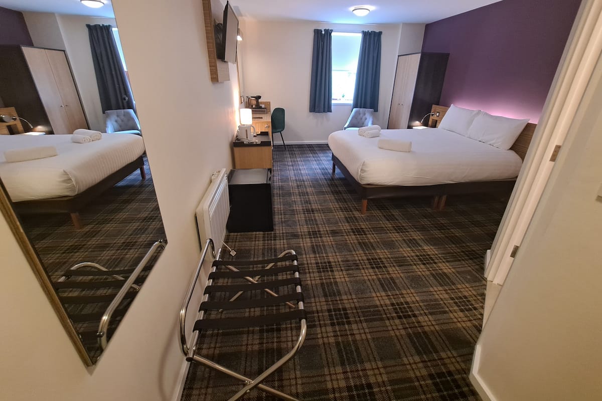 A hotel room with two beds, a small kitchenette, a mirror, and a view of the outside through a window.