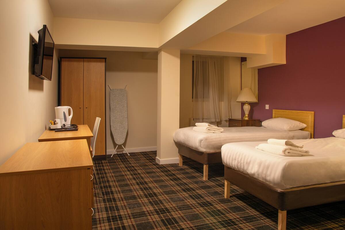 A hotel room with two beds, a desk, a television, and a shower area.