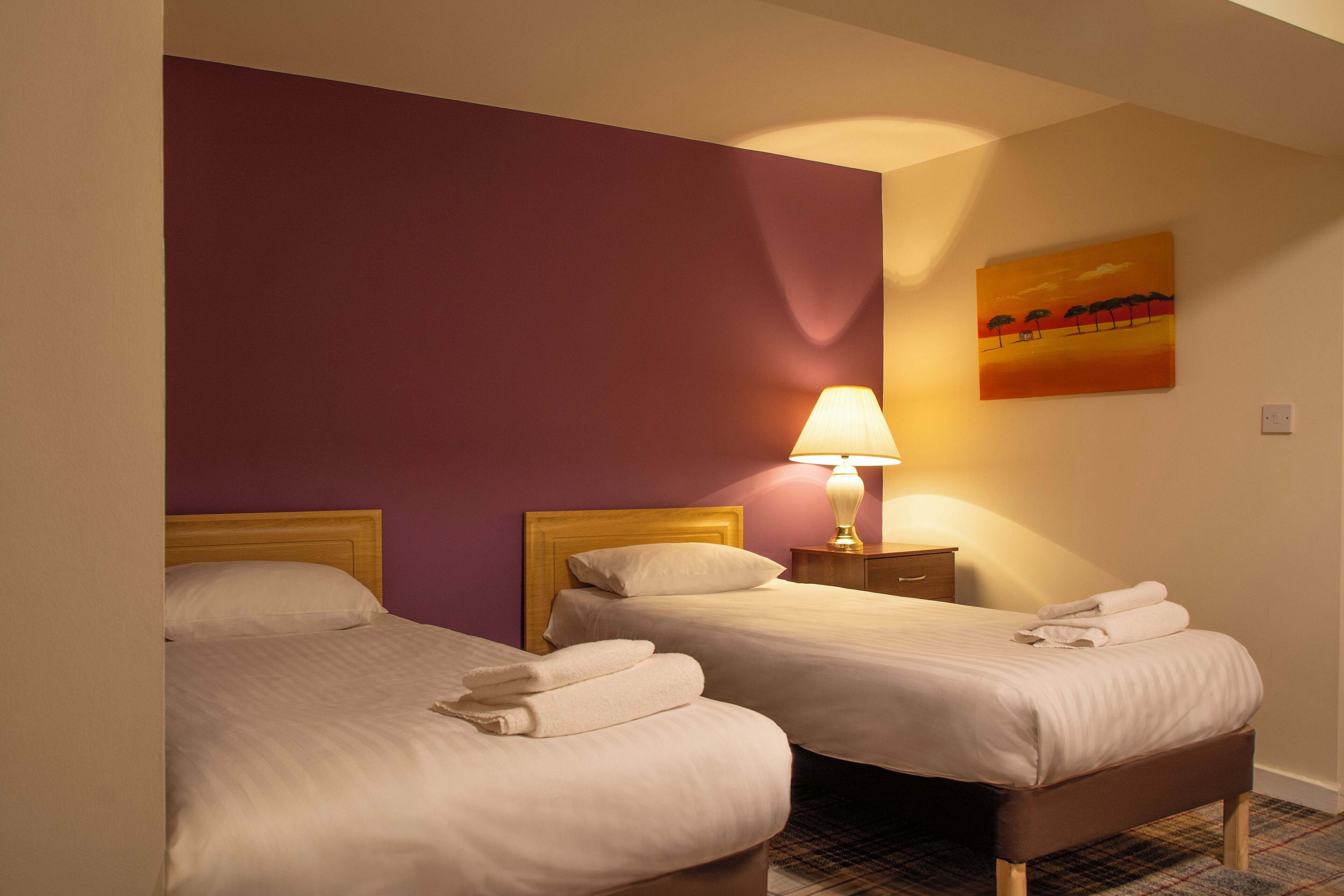 Une chambre d’hôtel avec deux lits, une table de chevet avec une lampe et un tableau au mur.