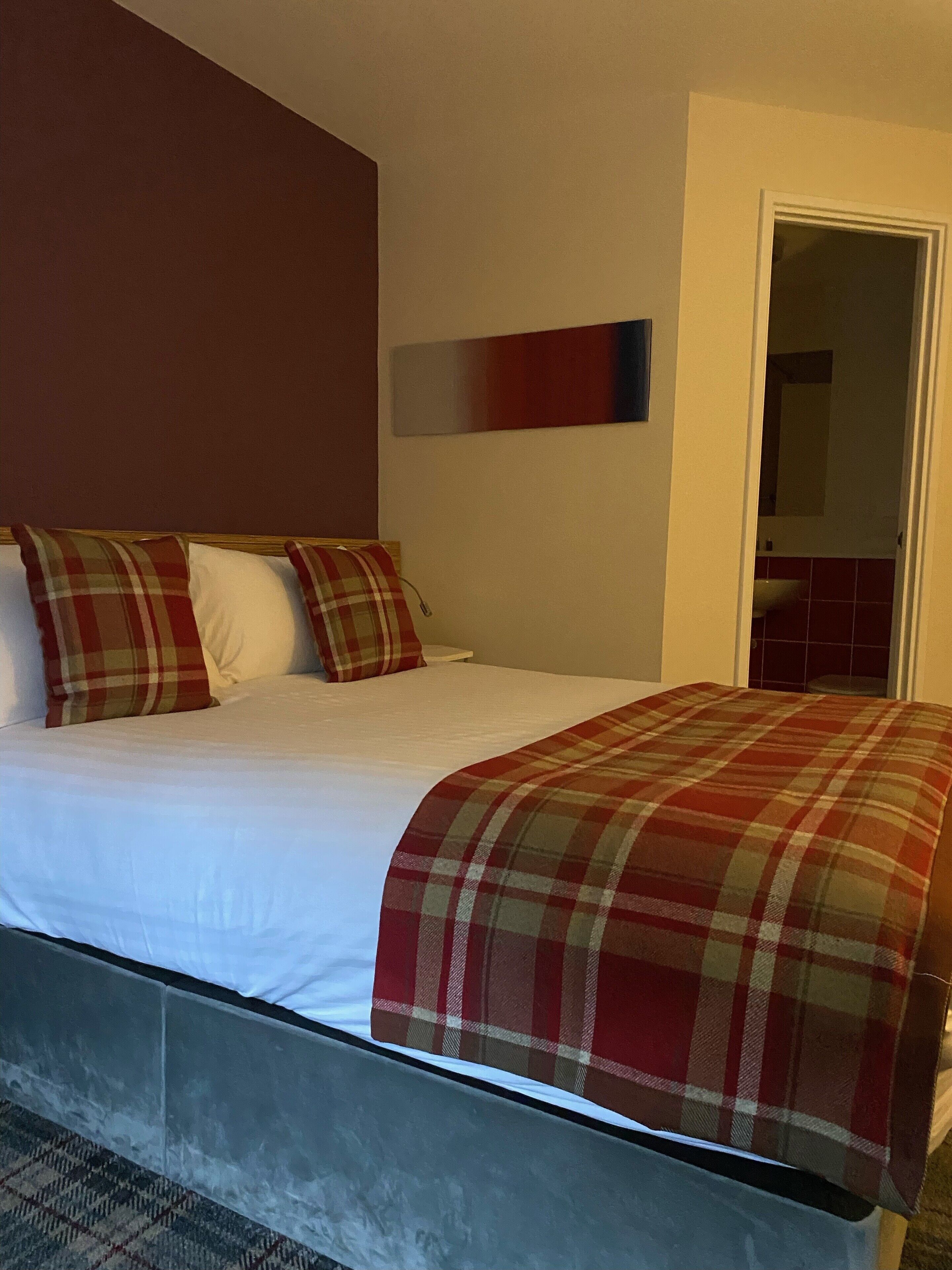 A bed with a plaid blanket, white pillows, and a red accent wall.