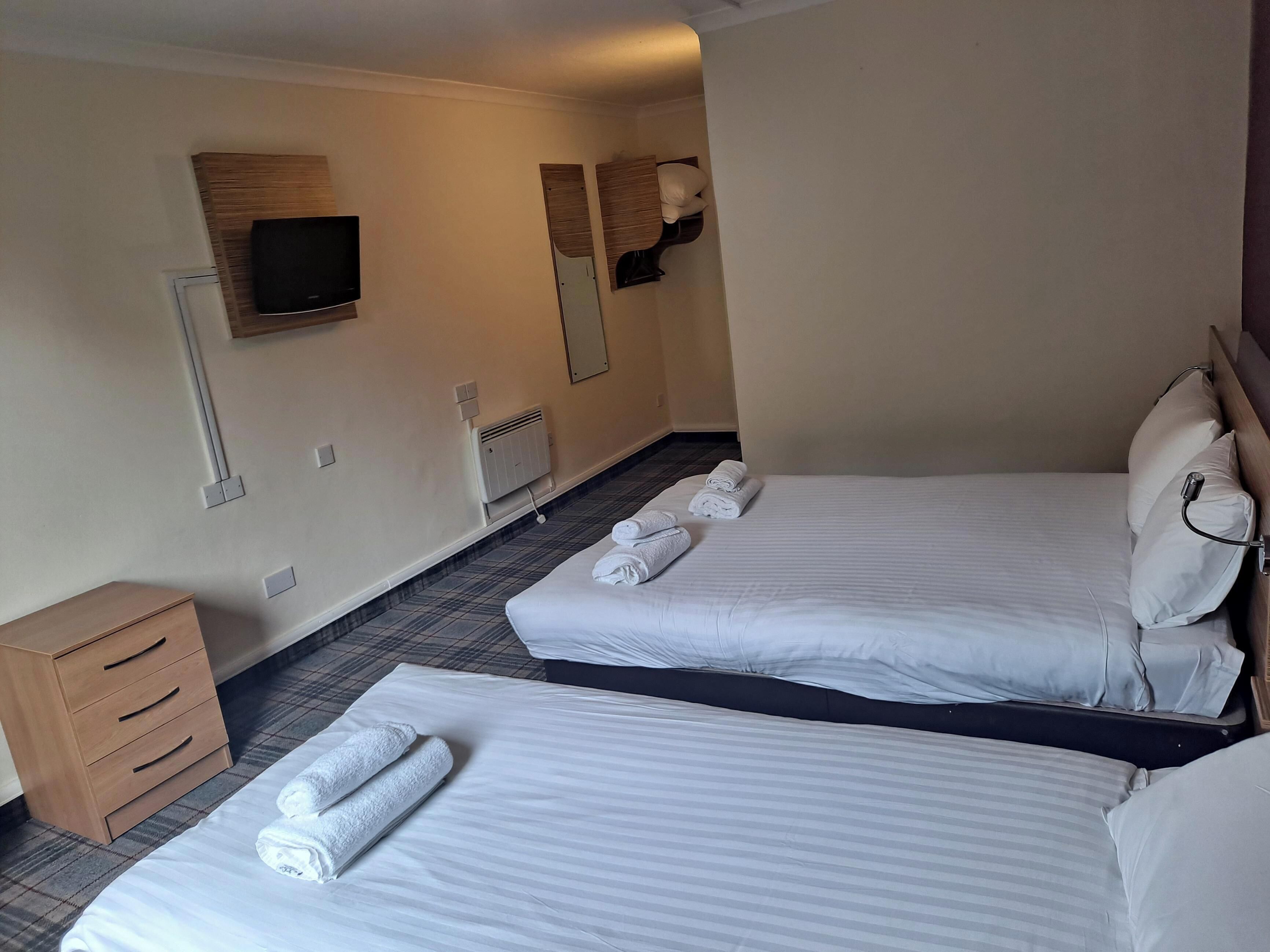 A hotel room with two beds, a TV, a heater, and a wooden dresser.