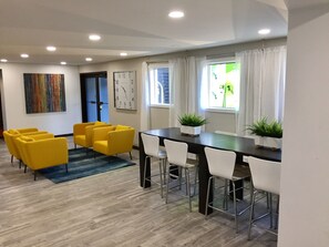 A modern dining area with a wooden table, white chairs, and yellow armchairs. There is a clock on the wall and a window with curtains. - Days Inn & Suites by Wyndham Cincinnati North (Cincinnati)