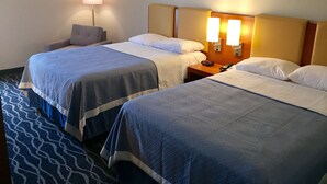 A hotel room with two beds, a nightstand with a phone, and a lamp.