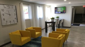 A hotel lobby with yellow armchairs, a large wall clock, a TV screen, and a staircase.