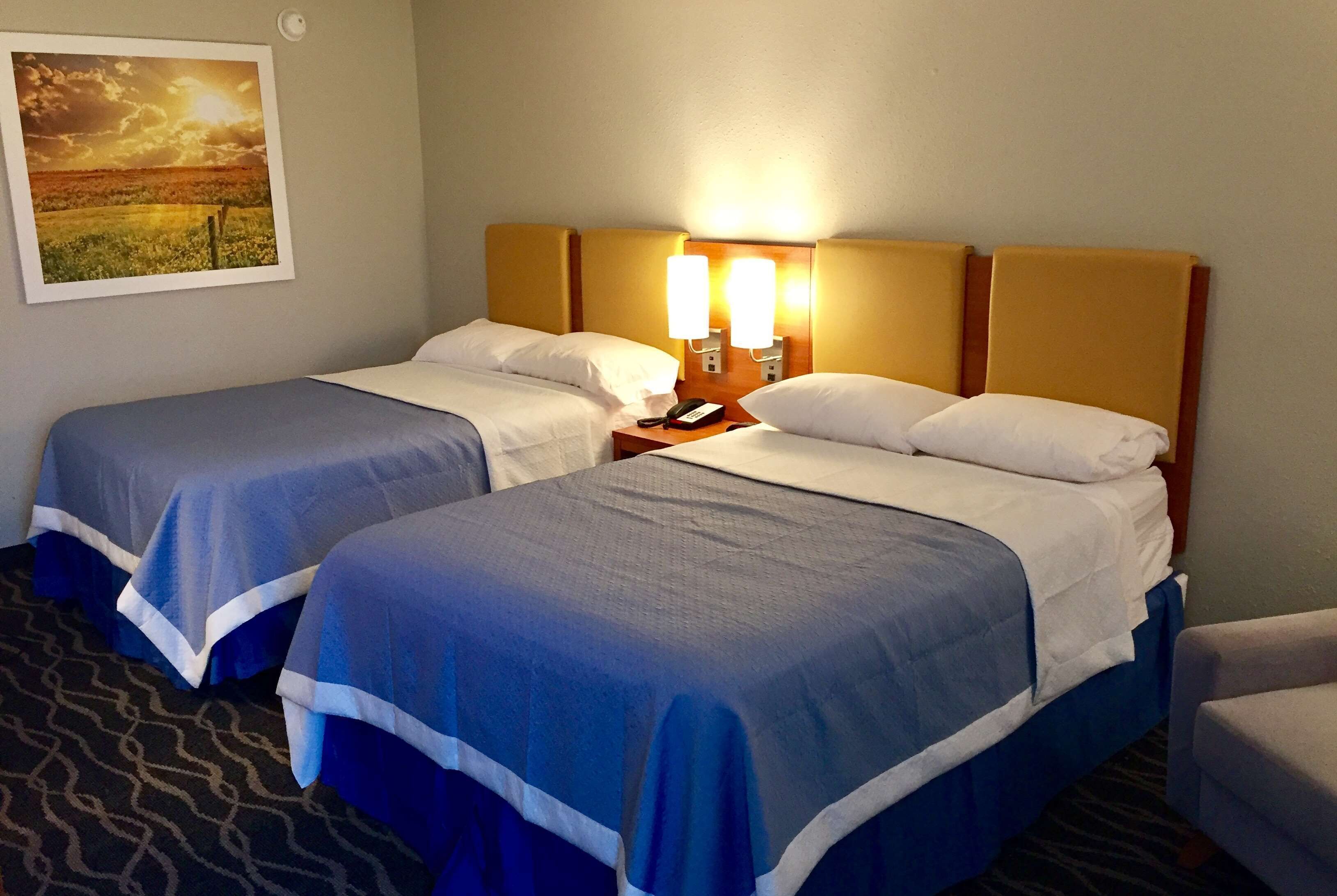 A hotel room with two beds, a nightstand with a phone, and a wall-mounted lamp.