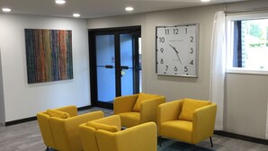 A modern waiting area with yellow chairs, a large clock, and a colorful abstract painting on the wall.