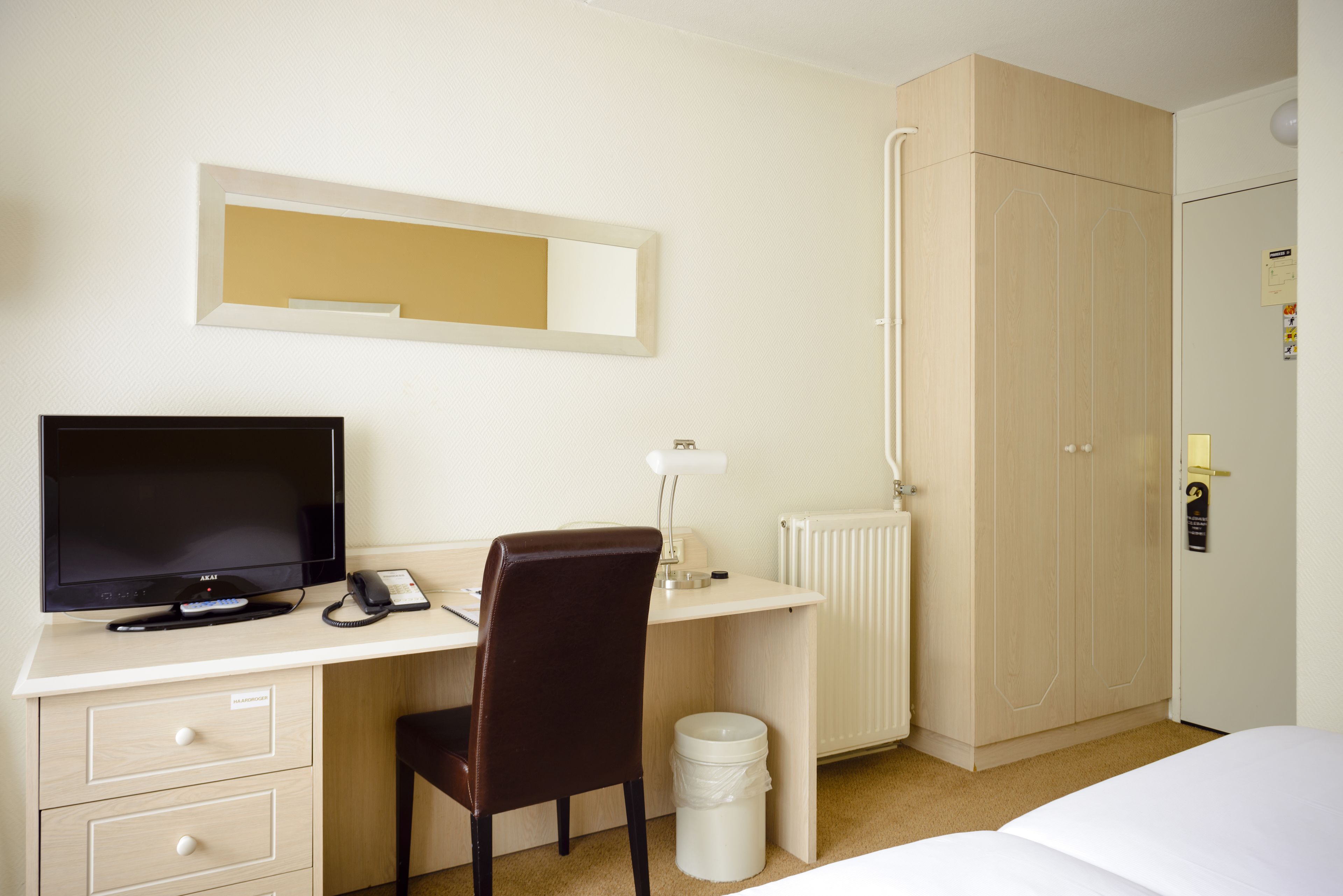 Een hotelkamer met een bureau, stoel, televisie en kledingkast.