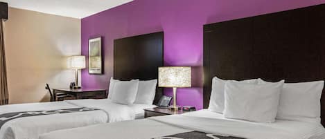 A hotel room with two beds, purple walls, and a nightstand with a lamp.