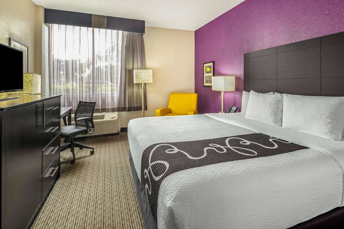 A hotel room with a large bed, a desk with a television, a chair, and a window with curtains.