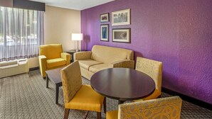 A hotel room with a purple accent wall, a yellow sofa set, a round table, and a ceiling fan. - La Quinta Inn & Suites by Wyndham Miami Lakes (Miami Lakes)