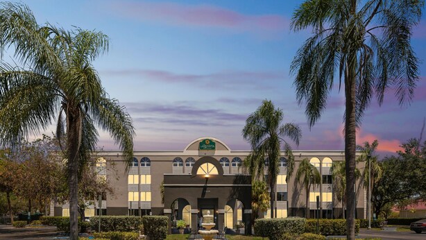 A hotel with a central fountain, palm trees, and a clear sky. - La Quinta Inn & Suites by Wyndham Miami Lakes (Miami Lakes)