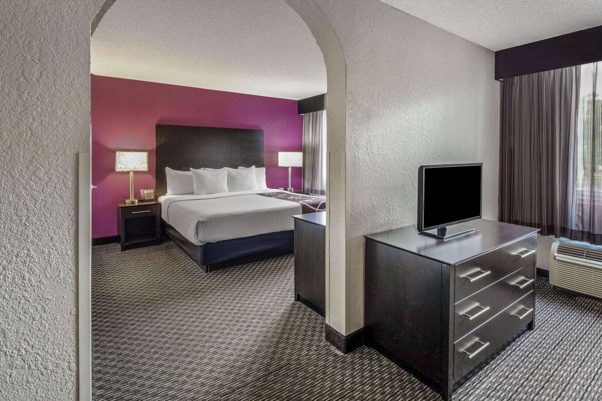 A hotel room with a large bed, a flat-screen TV, a dresser, and a nightstand with lamps.