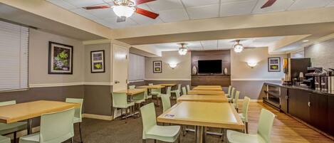 A dining area with multiple tables and chairs, ceiling fans, and wall-mounted light fixtures.