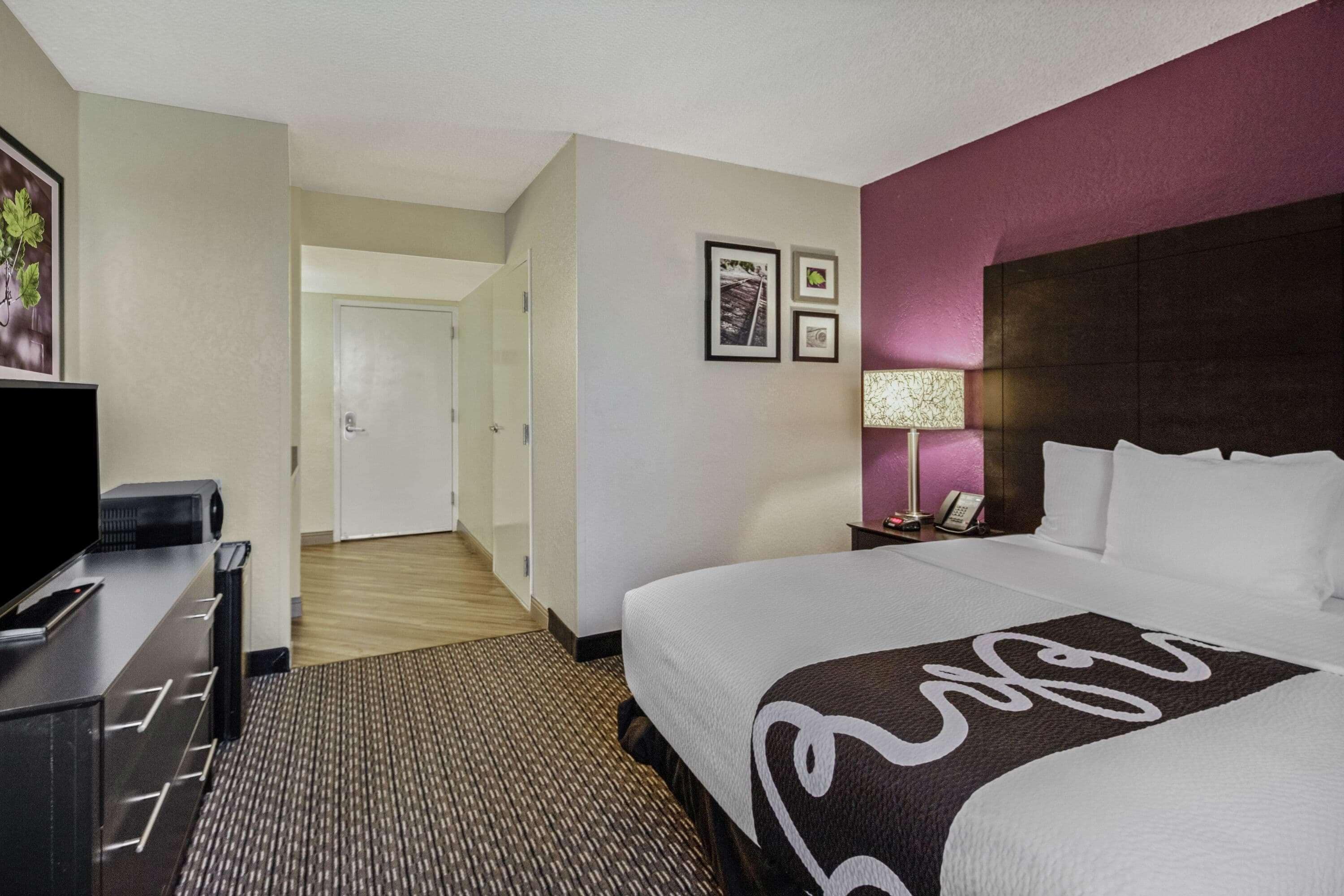 A hotel room with a large bed, a desk with a computer, a lamp, and framed pictures on the wall.