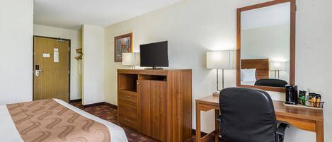 A hotel room with a bed, a desk with a computer, a chair, a TV, and a mirror.