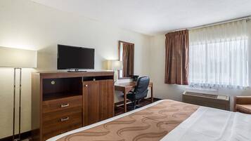 Une chambre d’hôtel comprenant un lit, un bureau avec une chaise, une télévision, un miroir et une fenêtre avec des rideaux.