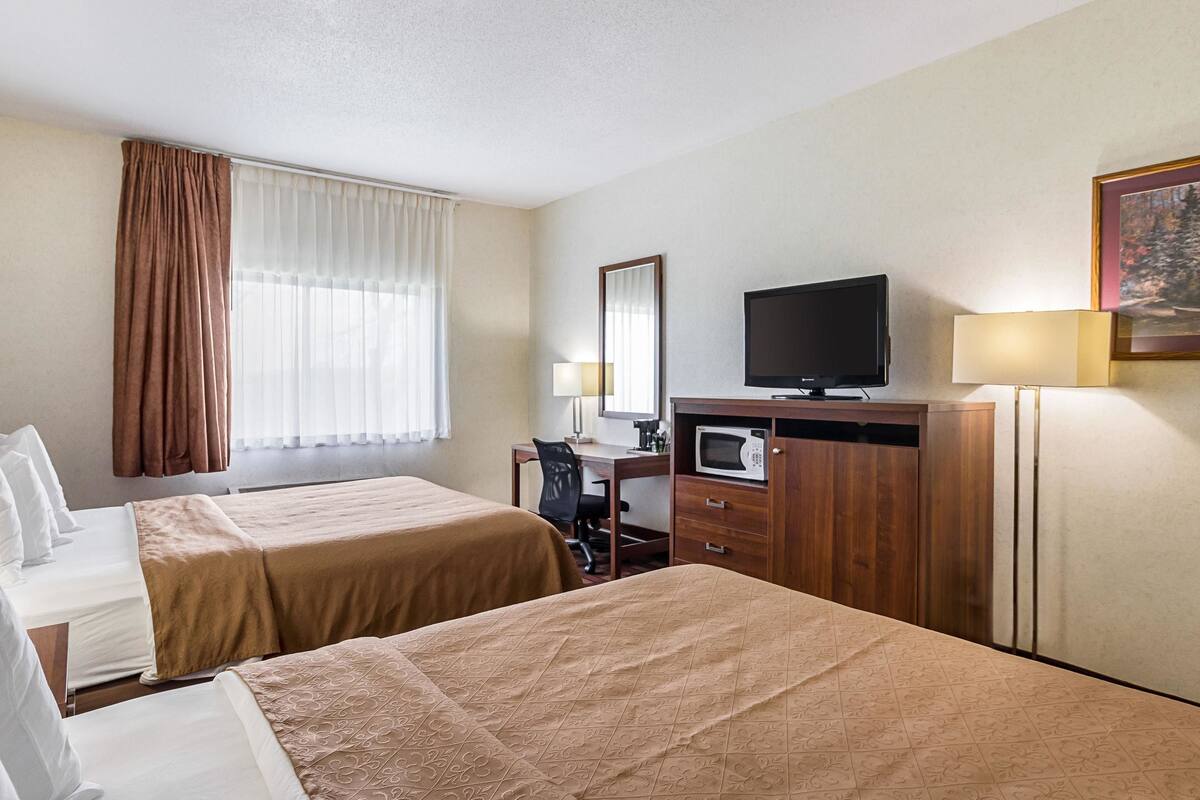 A hotel room with two beds, a desk with a chair, a television, a microwave, and a lamp.