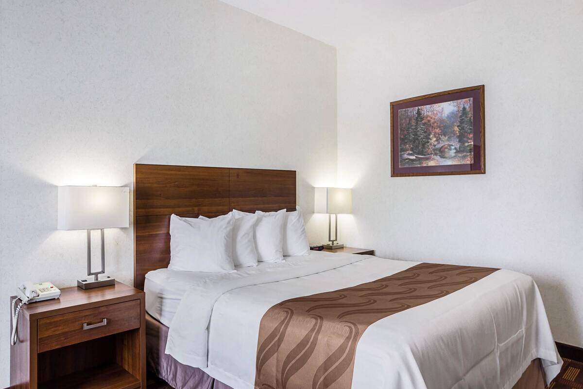 A neatly made bed with a wooden headboard, two bedside lamps, a nightstand with a phone, and a framed picture on the wall.