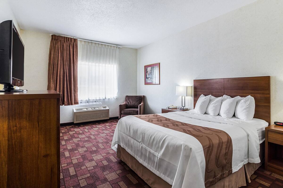 A hotel room with a bed, a television, a chair, a desk, and a window with curtains.