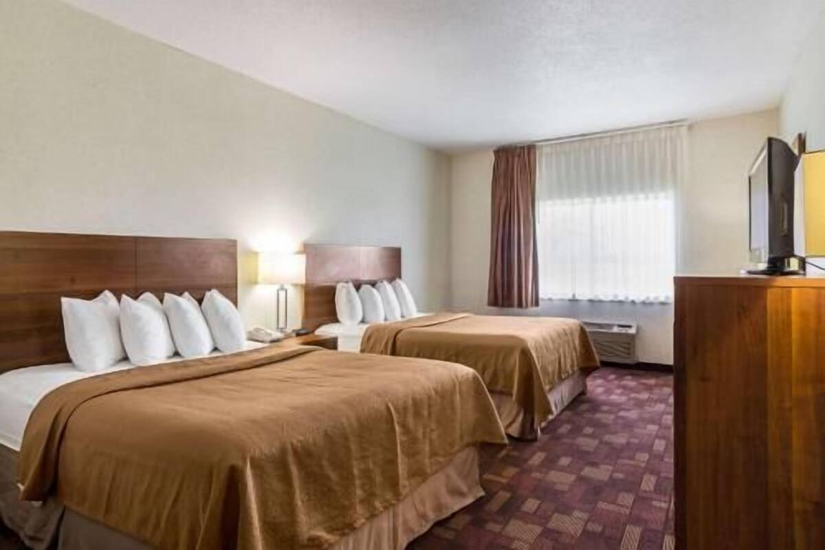 A hotel room with two beds, a desk, a lamp, and a television.