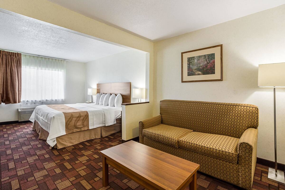 A hotel room with a bed, a sofa, a table, and a painting on the wall.