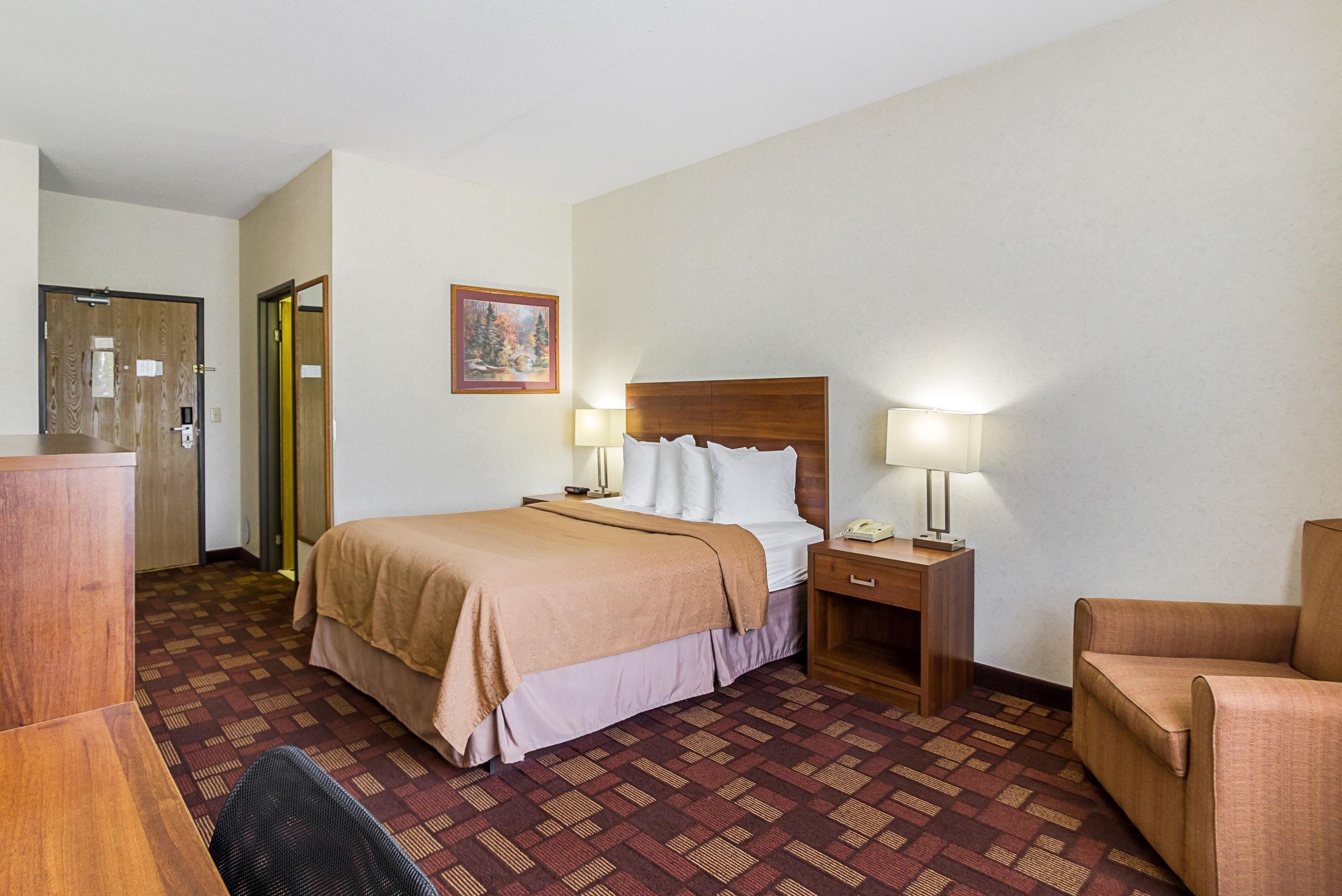 Une chambre d’hôtel comprenant un lit, deux tables de chevet avec des lampes, une chaise, un bureau et une porte.