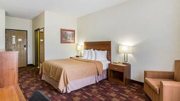 Une chambre d’hôtel comprenant un lit, deux tables de chevet avec des lampes, une chaise, un bureau et une porte.