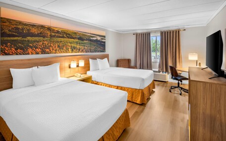 A hotel room with two beds, a desk, a chair, a television, and a large landscape painting on the wall.