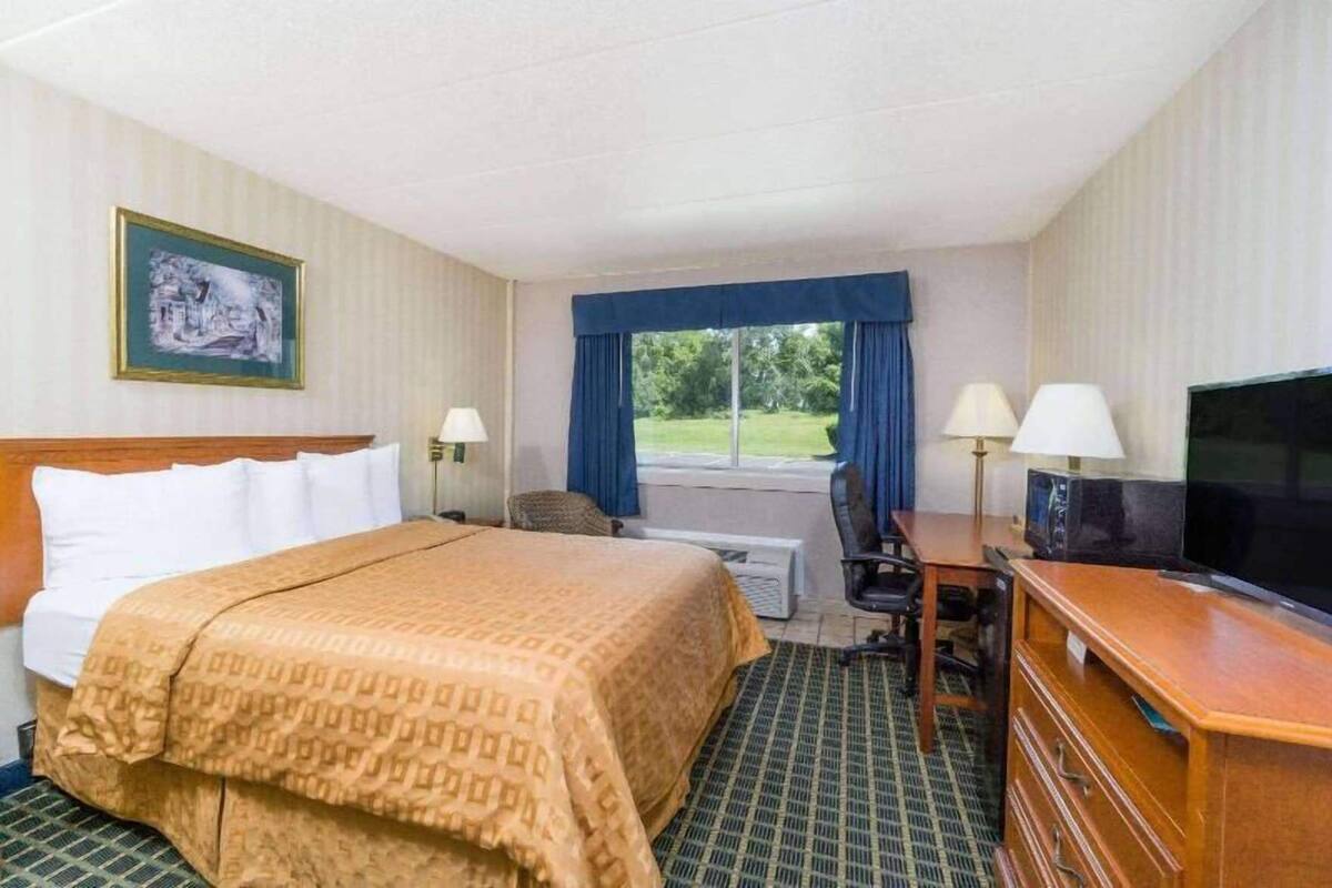 A hotel room with a bed, desk, television, and a window with curtains.