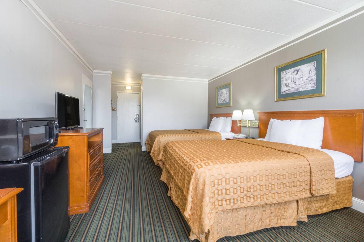 A hotel room with two beds, a TV, a dresser, and a door leading to the bathroom.