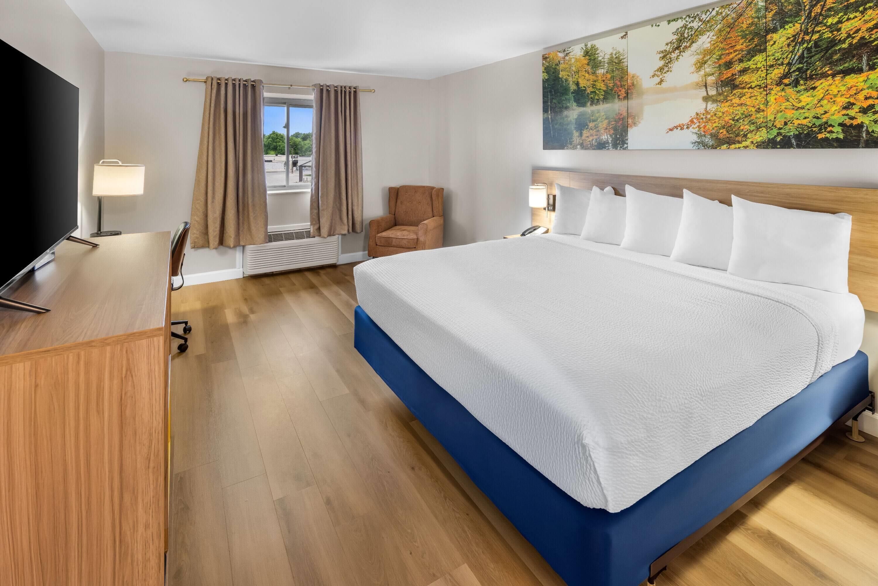 A hotel room with a large bed, a desk, a chair, a TV, and a window with curtains.