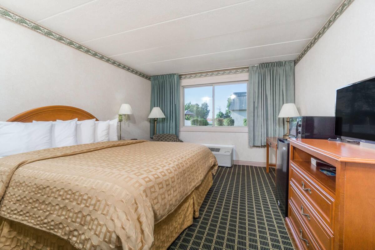 A hotel room with a bed, a television, a dresser, and a window with curtains.