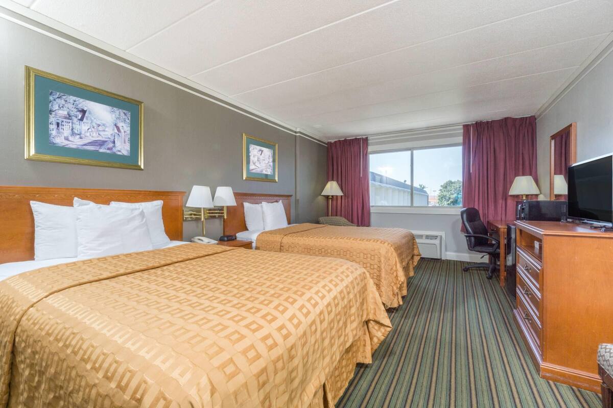 A hotel room with two beds, a desk, a television, and a window with curtains.