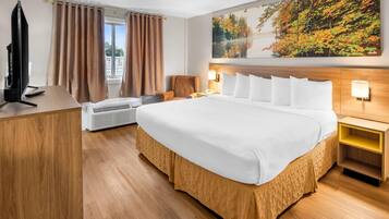 A hotel room with a large bed, a desk with a computer, an air conditioner, and a painting of autumn leaves on the wall.