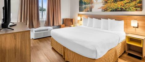 Ein Hotelzimmer mit einem großen Bett, einem Schreibtisch mit Computer, einer Klimaanlage und einem Wandbild von Herbstlaub.